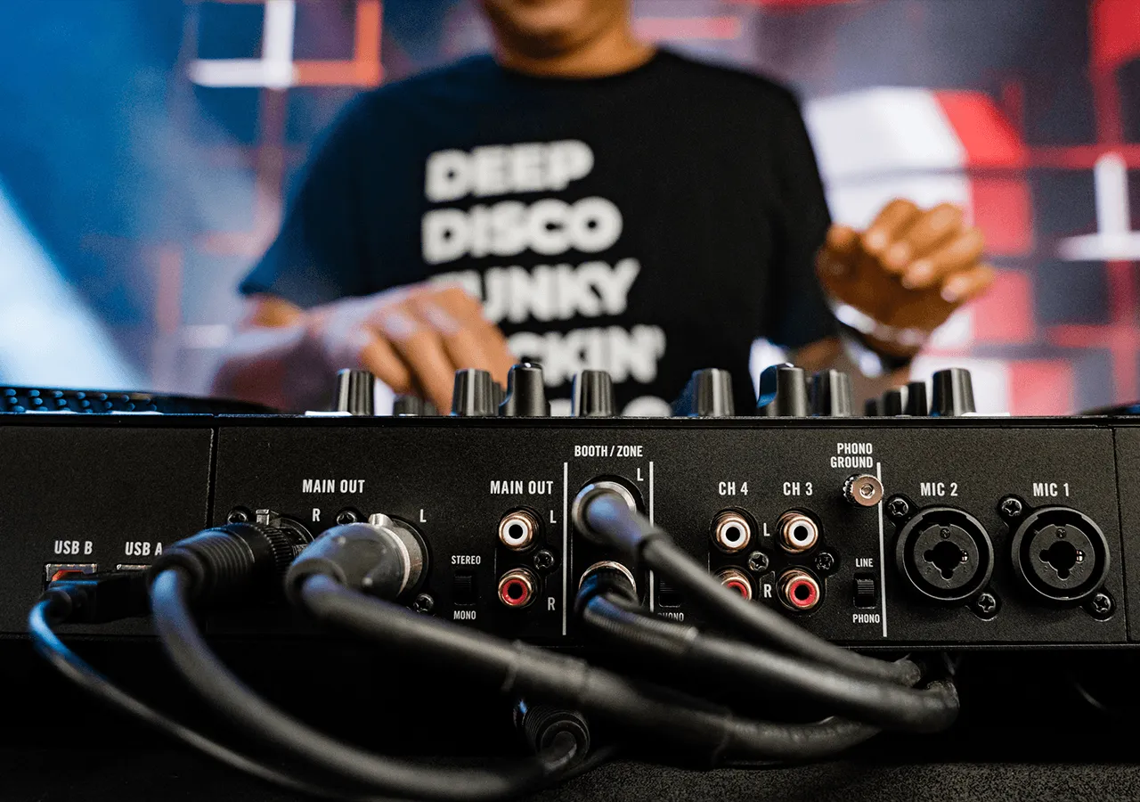 Controlador DJ Rane Four - Calidad Rane vista de la controladora desde la parte de atrás con detalle de algunas conexiones y sobre ella se ve el torso de un DJ con las manos en la zona de canales