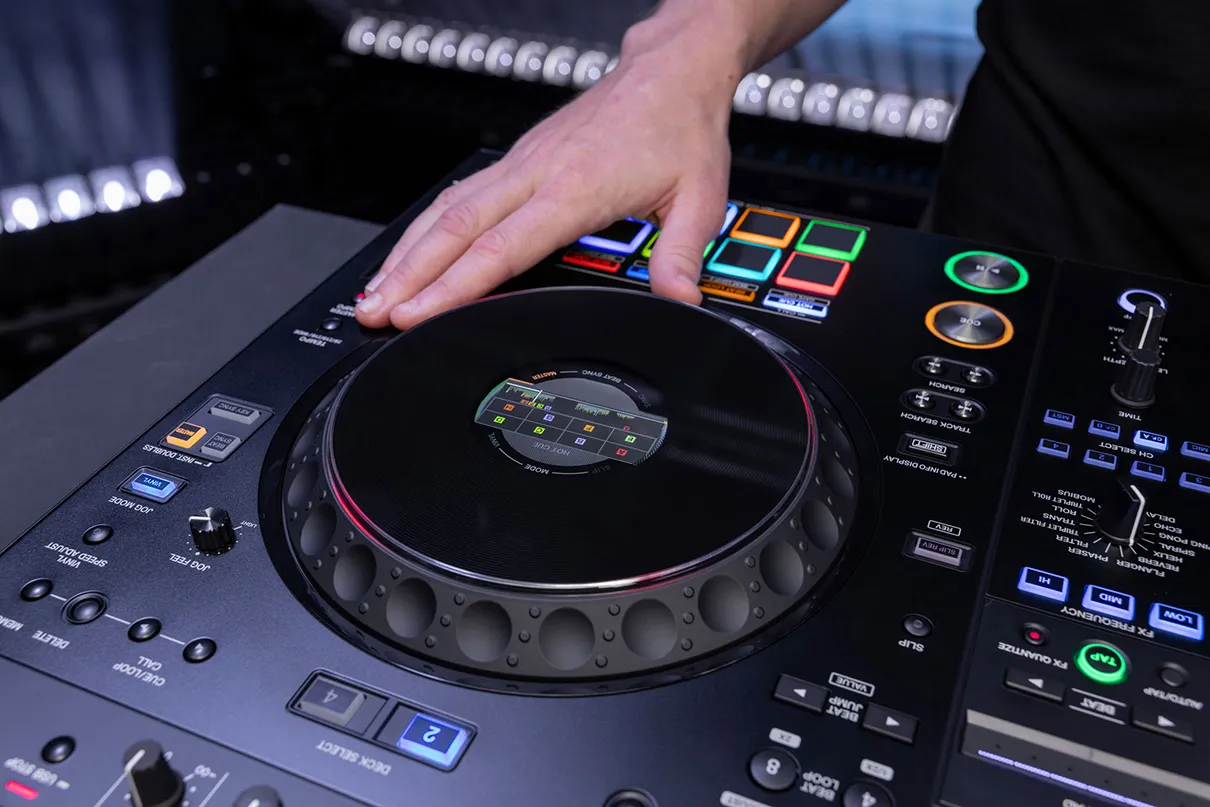 Primer plano de mano de DJ realizando scratch sobre el jog wheel dorado del AlphaTheta XDJ-AZ-N con pantalla central On-Jog Display.