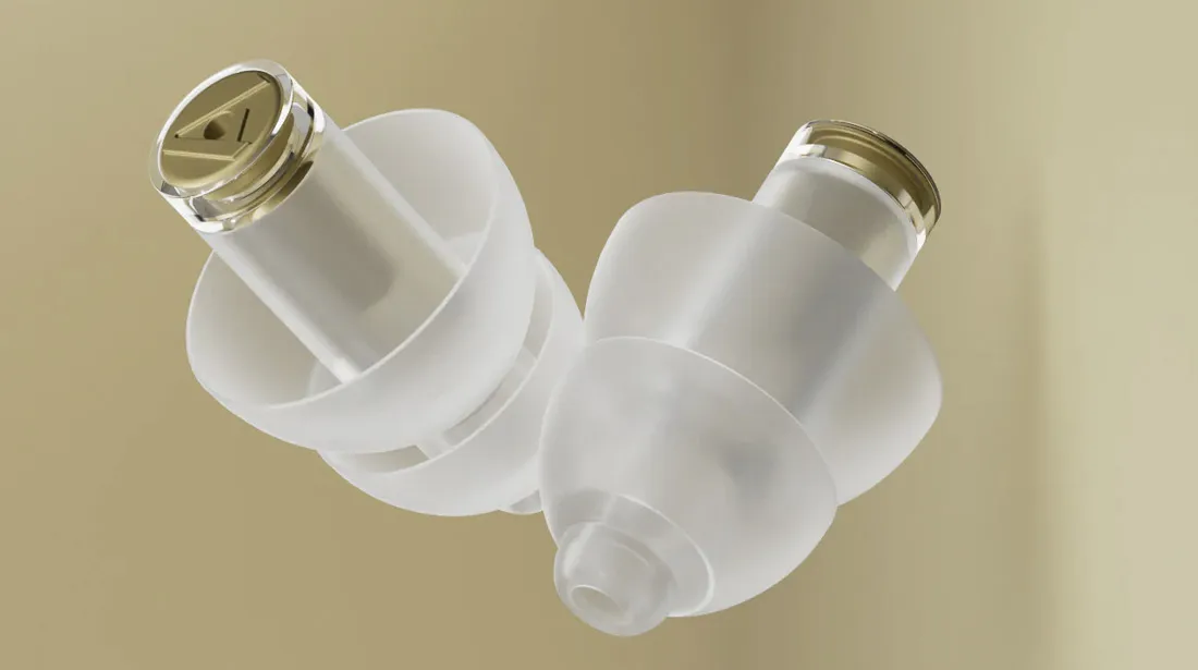 Plano macro detallado de dos tapones auditivos de silicona transparente Alpine MusicSafe Pro, mostrando los filtros de protección dorados integrados y su estructura flexible multilaminar.